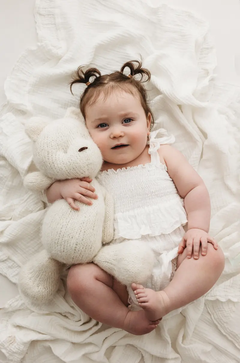 Baby laying on a blanket holding a white teddy